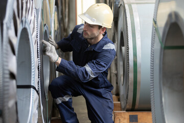 Factory worker inspects steel coils in an industrial warehouse, representing metal manufacturing, quality control, material inspection, workplace safety, production operations. © eakgrungenerd
