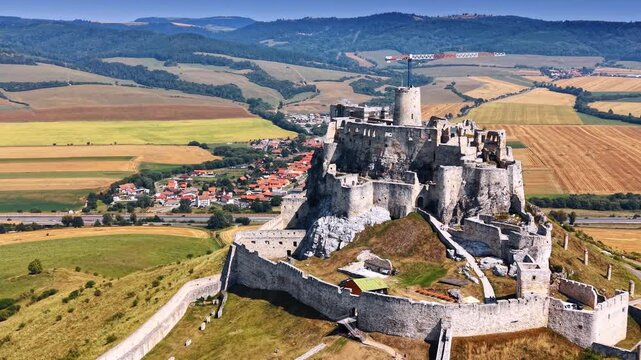 Stone tower and ruins of Spis Castle. Ancient medieval fortress stands on a rocky hill with surrounding farmland in the background.
