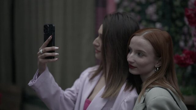 Two young women happily take selfies together with a smartphone outdoors. They are enjoying their friendship and capturing fun moments.