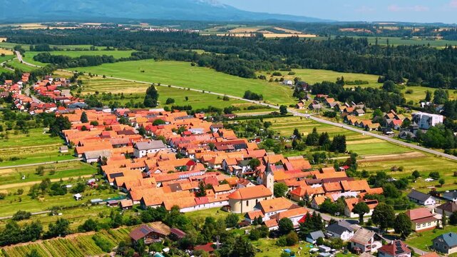 Aerial view of a village with red rooftops, Slovakia. High angle drone shot of European houses, church tower, green pastures, and distant forest in Liptov.