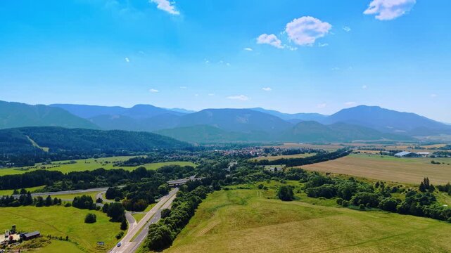 Aerial view of a highway cutting through valley landscape, Slovakia. High angle shot of asphalt road, green meadows, pine forest, and mountain ridge in Liptov region.