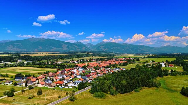 Aerial view of a valley village near alpine ridge, Slovakia. High angle landscape of a countryside town, asphalt road, pine forest, and mountain peaks in Liptov region.
