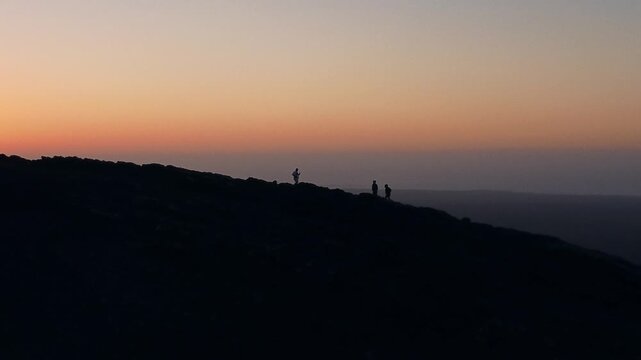 Silhouettes of hikers walking along a mountain crest during a colorful and serene sunset