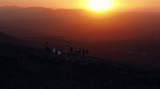 Silhouettes of a group of friends admiring the sun setting behind a vast volcanic landscape