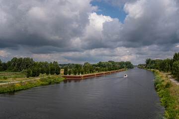 Fototapeta premium Wide view of canal shipping route with steel sheet pile wall along bank under cloudy sky in Brandenburg Germany with copy space