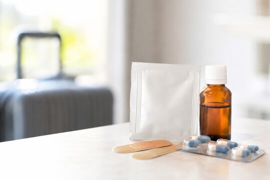 Medicamentos y suministros sobre una mesa cerca de una maleta en un ambiente de vivienda