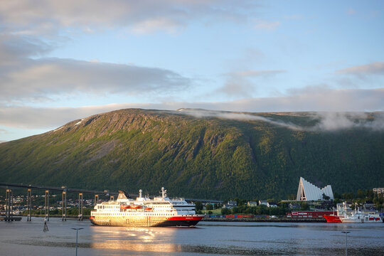 Tromso, Norway, June 19th 2026: A Hurtigruten ship lies alongside the harbor in Troms&oslash;, with the striking Arctic Cathedral rising across the water, capturing the unique blend of maritime heritage	