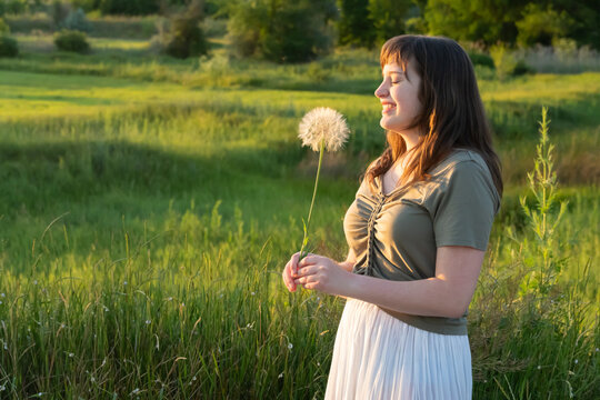 Happy young woman holding dandelion in summer meadow