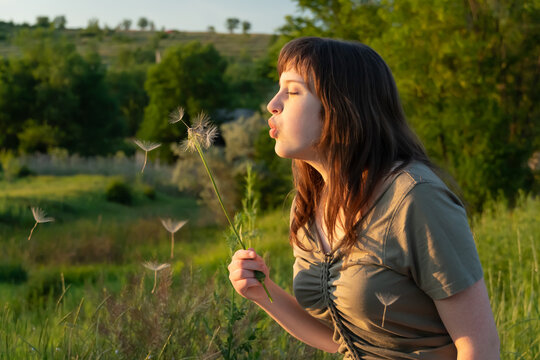 Young woman blowing dandelion seeds in a sunny meadow