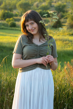 Young Woman Holding Wild Flower in Summer Meadow at Golden Hour