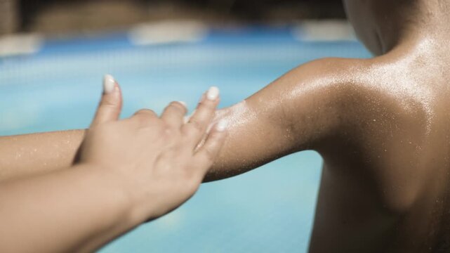 Mother applying sunscreen cream on child's arm by the pool, summer skin protection