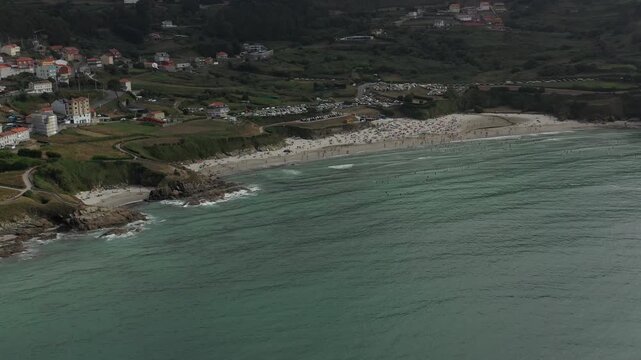 Aerial view of the sandy beach and turquoise waters at Caion, with green coastal hills and a parking area in the background, Caion, A Coruna, Spain.