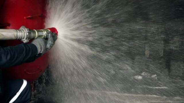 Close-up of firefighter operating a hose nozzle and spraying a powerful stream of water under pressure. Fire suppression, emergency response and firefighting equipment.