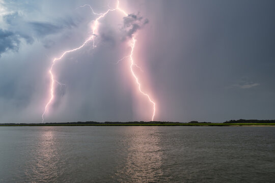 Lightning strikes over Beaufort SC during a storm with dark clouds and a river in the foreground