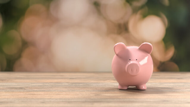 Pink piggy bank sitting on a wooden surface, showing financial savings and monetary growth concepts with a blurred green outdoor garden bokeh background