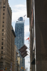 Fototapeta premium narrow view of Yonge St with flag banners outside Moores Clothing for Men, old office towers and (at center) L-Tower condominium and beyond that SkyTower, Toronto
