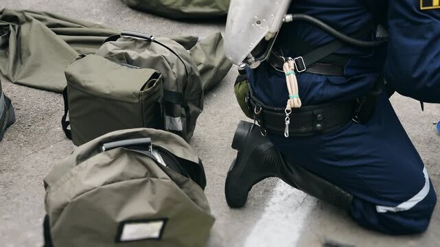 Firefighter in protective gear kneeling beside bags of emergency equipment. Professional rescue gear prepared for firefighting and emergency response operation.