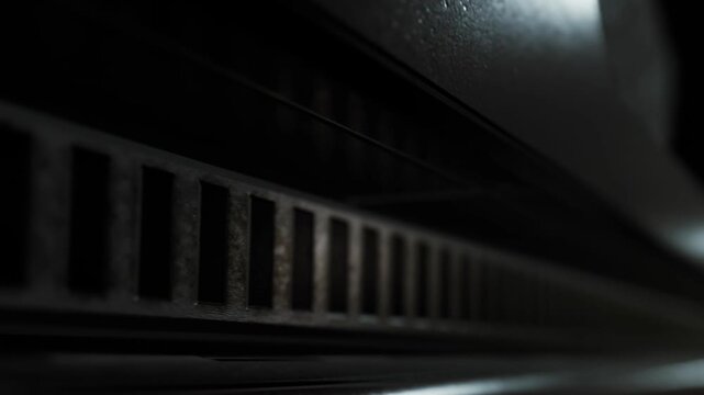 A close view of a black vent shows its grille pattern and texture. The scene captures light reflecting off the surface. The setting appears to be indoors with soft lighting.