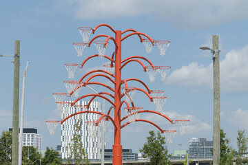 Fototapeta premium view of Alexandre Arrechea's Orange Functional, 2022, composed of steel and basketball nets, #1, in the plaza of Old Firehall 30, at Biidaasige Park, Port Lands, Toronto