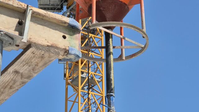 Tower crane lifting concrete bucket being guided and positioned on a building construction site.