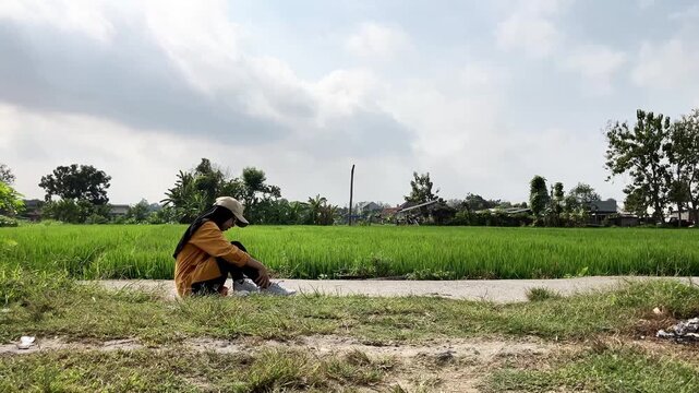 Slow motion video of a young Muslim woman in a hijab standing up and limping after suffering a sprained ankle. She walks with difficulty on a path next to a green rice field. Sports concept.