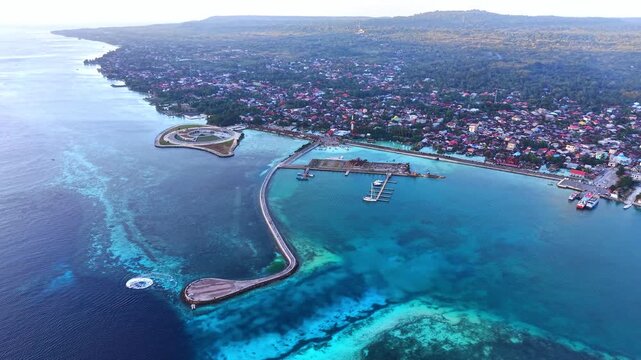 Aerial view of Marina Togo Wakatobi featuring a long pier extending into the clear turquoise waters of the coast in Kabupaten Wakatobi, Sulawesi Tenggara, Indonesia.