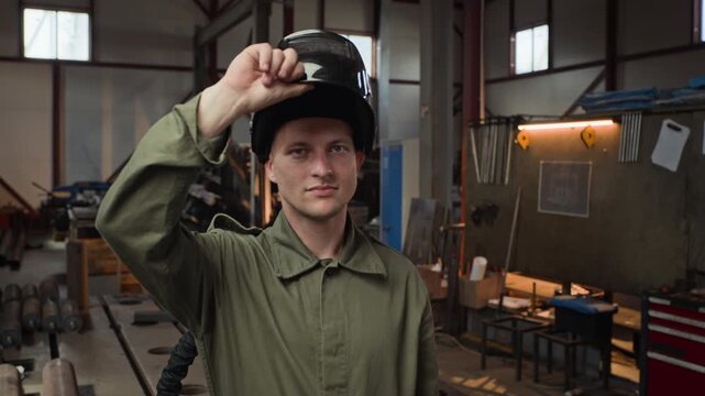 Portrait of Caucasian young adult male welder lifting protective mask in slow motion inside industrial workshop. Clip is perfect for industrial safety and vocational training campaigns