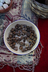 Wild edible snails in an enamel bowl prepared for cooking traditional Cretan chochlioi boubouristoi. Rustic local Greek delicacy display on a woven traditional table runner setup. © MairhLu