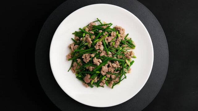 Stir-fried flowering garlic chives with minced pork in white plate.Top view.	