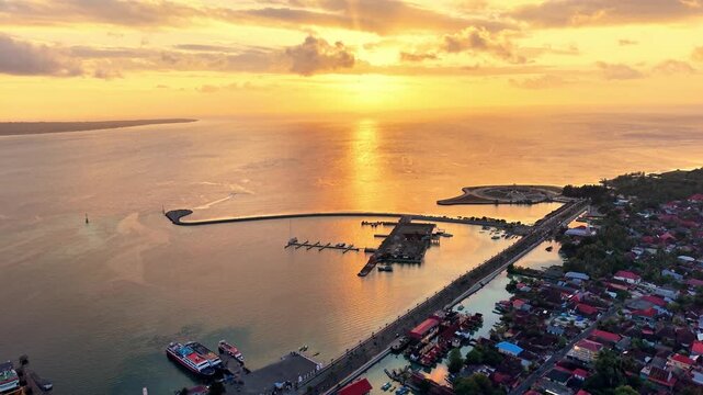 Aerial view of Marina Togo Wakatobi at sunset with boats docked in the harbour and coastal town buildings in Kabupaten Wakatobi, Sulawesi Tenggara, Indonesia.