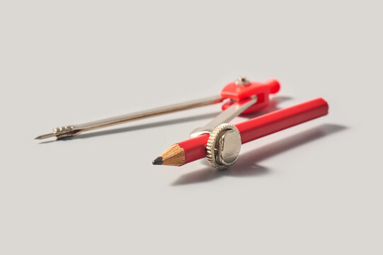 red geometry compass with pencil isolated gray background, metal and plastic drafting tool with sharp point in soft focus, close-up side view