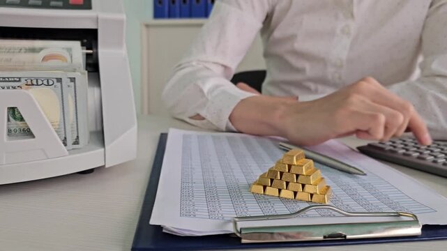 Counting gold bars and handling cash in an office setting with a calculator