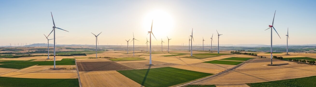 Aerial view of wind turbines in a wind farm set against a golden sunset over agricultural fields in Hangen-Weisheim, Rhineland-Palatinate, Germany.
