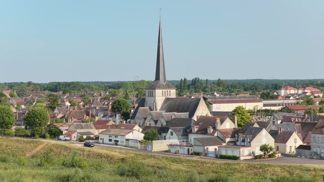 The picturesque village of Sully-sur-Loire in France, featuring a prominent historic church with a tall spire at the center, surrounded by traditional houses, aerial view.