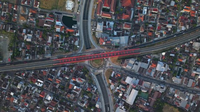 Aerial view of the red Joglo Railway Bridge crossing over a roundabout and urban neighborhood in Kecamatan Banjarsari, Jawa Tengah, Indonesia.
