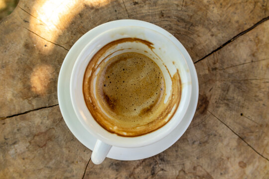 Top view of a freshly finished espresso in a white ceramic cup on a rustic wooden table, highlighting rich coffee crema, warm natural light, and a cozy outdoor cafe atmosphere.