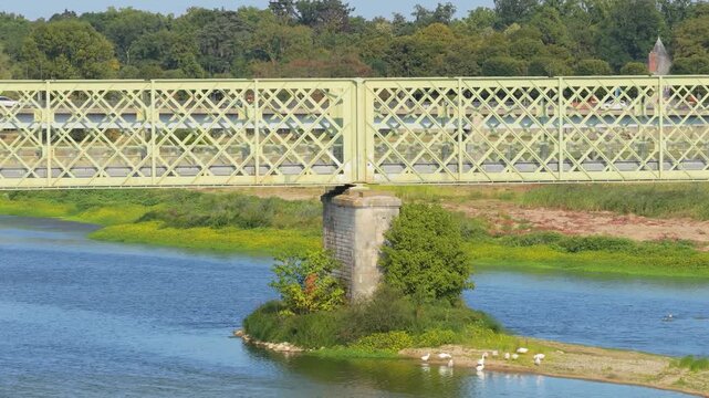 A static daytime shot of a pale green iron bridge spanning the Loire River in Sully sur Loire, France.