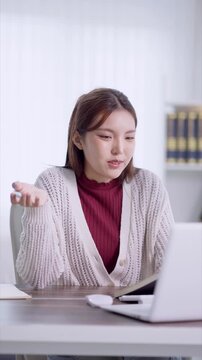 Young Asian woman thinking while taking online course at desk in bright home office with copy space