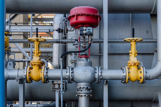 Close-up of yellow gate valves and a red actuator control valve installed on gray steel pipelines with flanges and instrumentation at a petrochemical industrial plant.