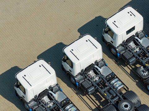 Aerial view of three white truck chassis parked in a row on a paved lot, Poland.