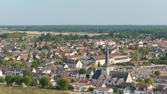 Sully-sur-Loire, France, showing a picturesque small town with traditional houses, a prominent church with a tall spire, tree-lined streets, and a cemetery, aerial view.