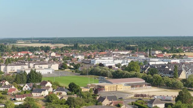 Sully-sur-Loire, France, showing a small town with residential houses, green spaces, and sports fields under a clear blue sky, aerial view.
