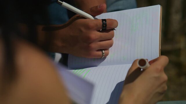 High school students are seen actively writing and drawing in their notebooks. Their hands are busy taking notes and sketching diagrams.