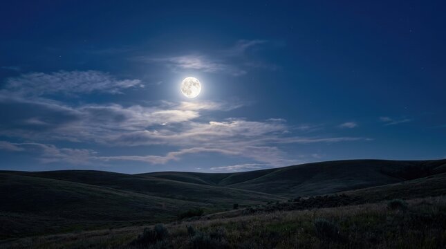A bright full moon dominates the dark night sky, illuminating a rolling landscape of hills and fields. Wispy clouds partially obscure the moon, creating a dramatic contrast between light and shadow.