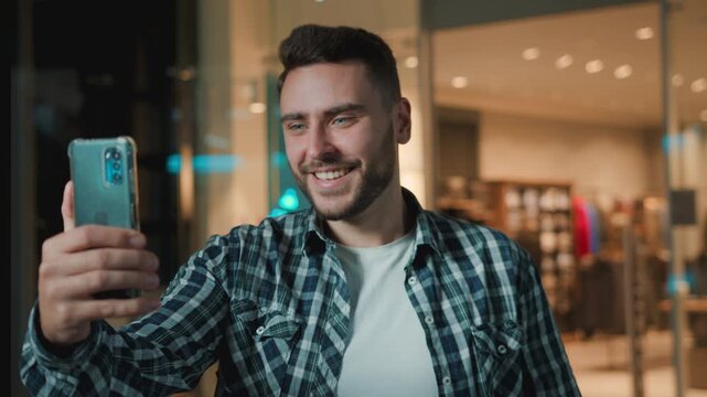 Happy cheerful Caucasian client man holding shopping bag take picture photo smiling posing for video call customer with purchase package smile male guy with smartphone conference in mall shop store