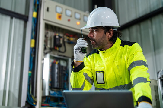 Professional electrical engineer using walkie-talkie and laptop computer for checking power control system in smart factory. Industrial maintenance and automation technology concept.