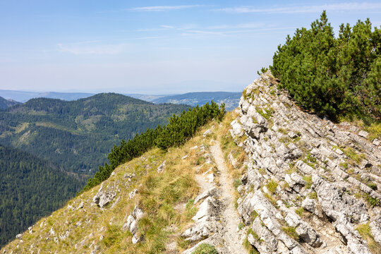 Narrow hiking path along rocky ridge with panoramic view of green mountain hills