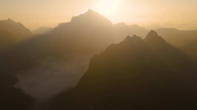 Aerial view of the volcanic peaks of Gunung Kelud rising above a sea of clouds during golden hour in Kecamatan Ngancar, Jawa Timur, Indonesia.