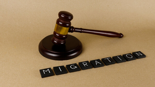 Wooden gavel standing beside black letter tiles spelling MIGRATION, symbolizing the legal frameworks and policies governing global human movement and immigration matters