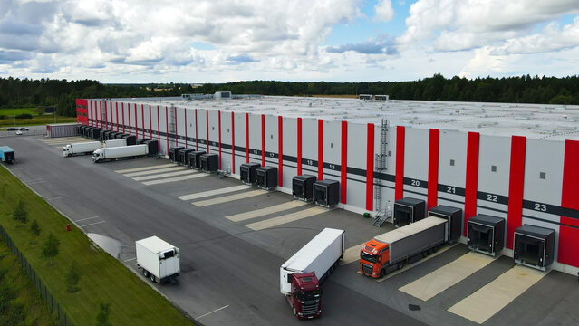 Large modern logistics center operating with numerous semi trailer trucks at loading docks, efficiently managing global supply chain distribution and freight transportation